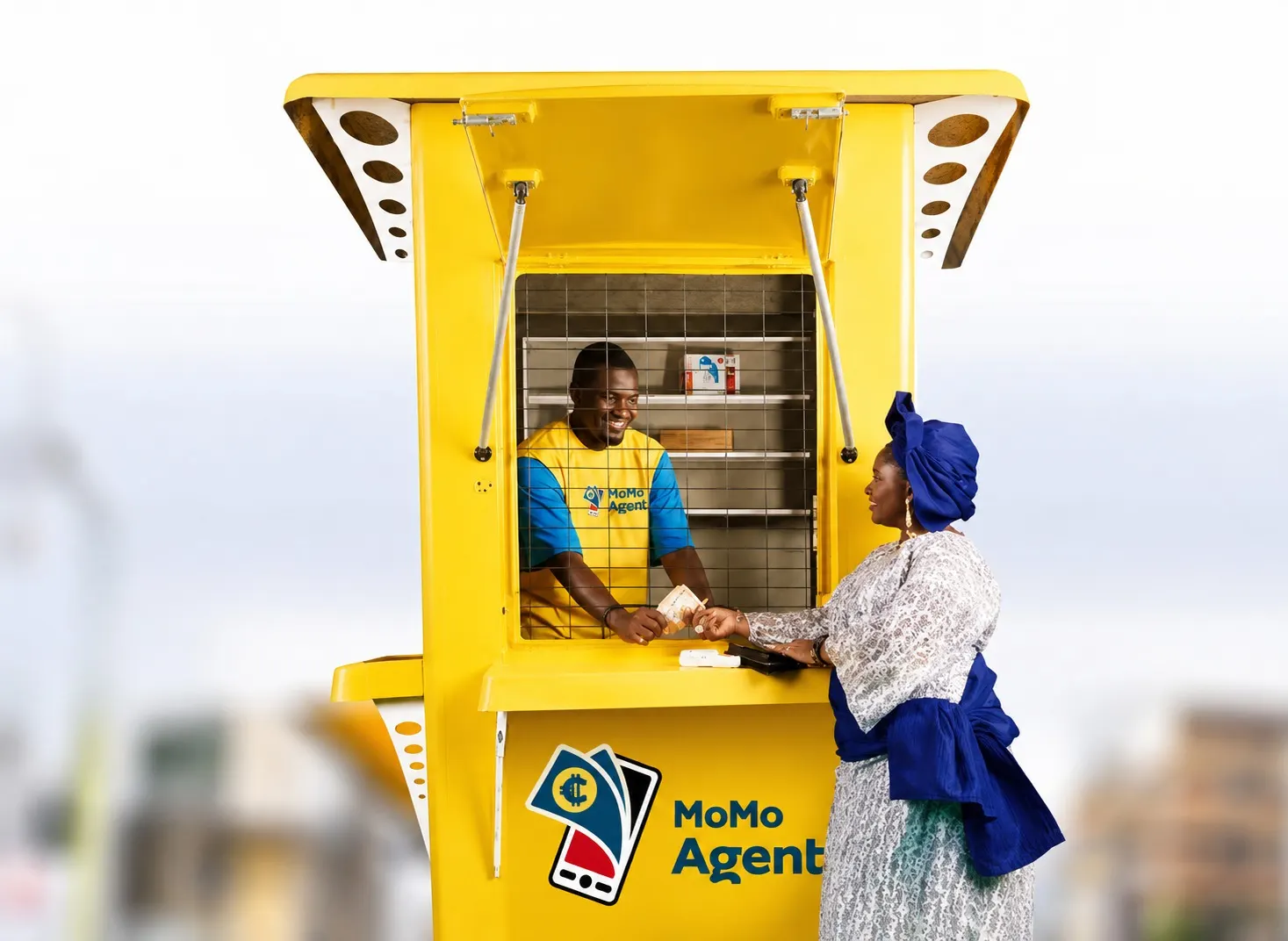 A MoMo agent at a yellow kiosk handing cash to a customer